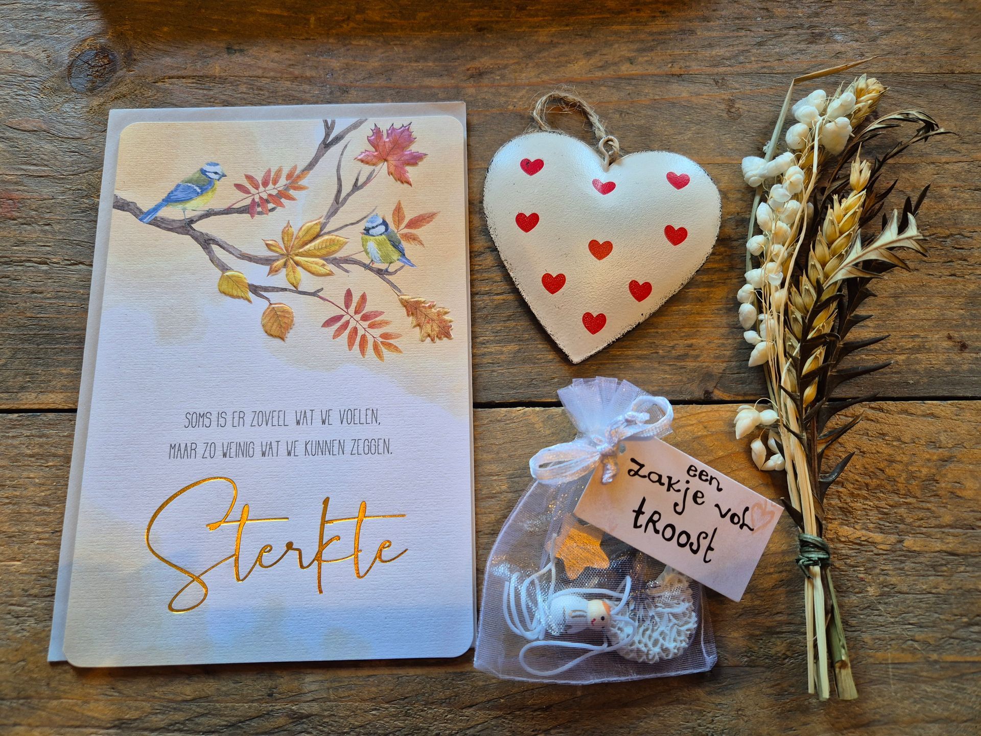 Cadeauverpakking met een notitieboekje met bloemenmotief, een hartvormige kaars, een snackzakje en gouden gedroogde bloemen, vastgebonden met een rood lint.