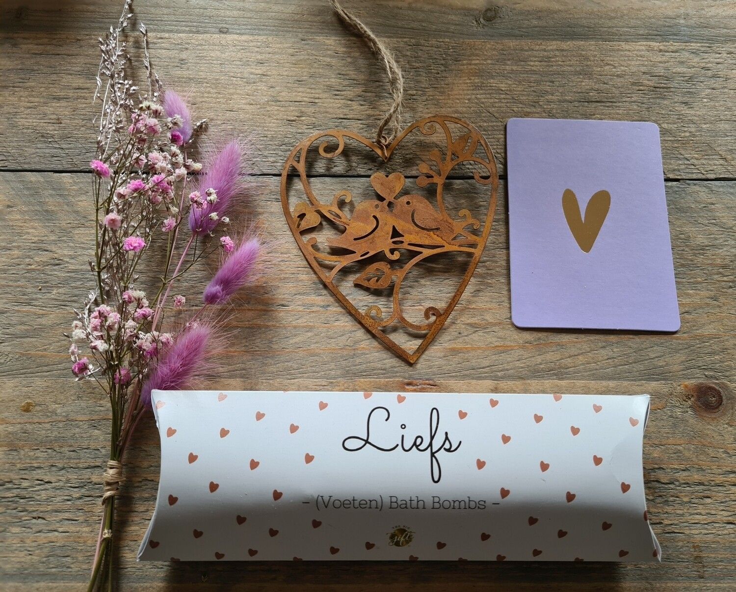 Cadeauverpakking met pastelkleurige bloemen, paarse kaart en gouden hartjesversiering op een achtergrond met stippen.