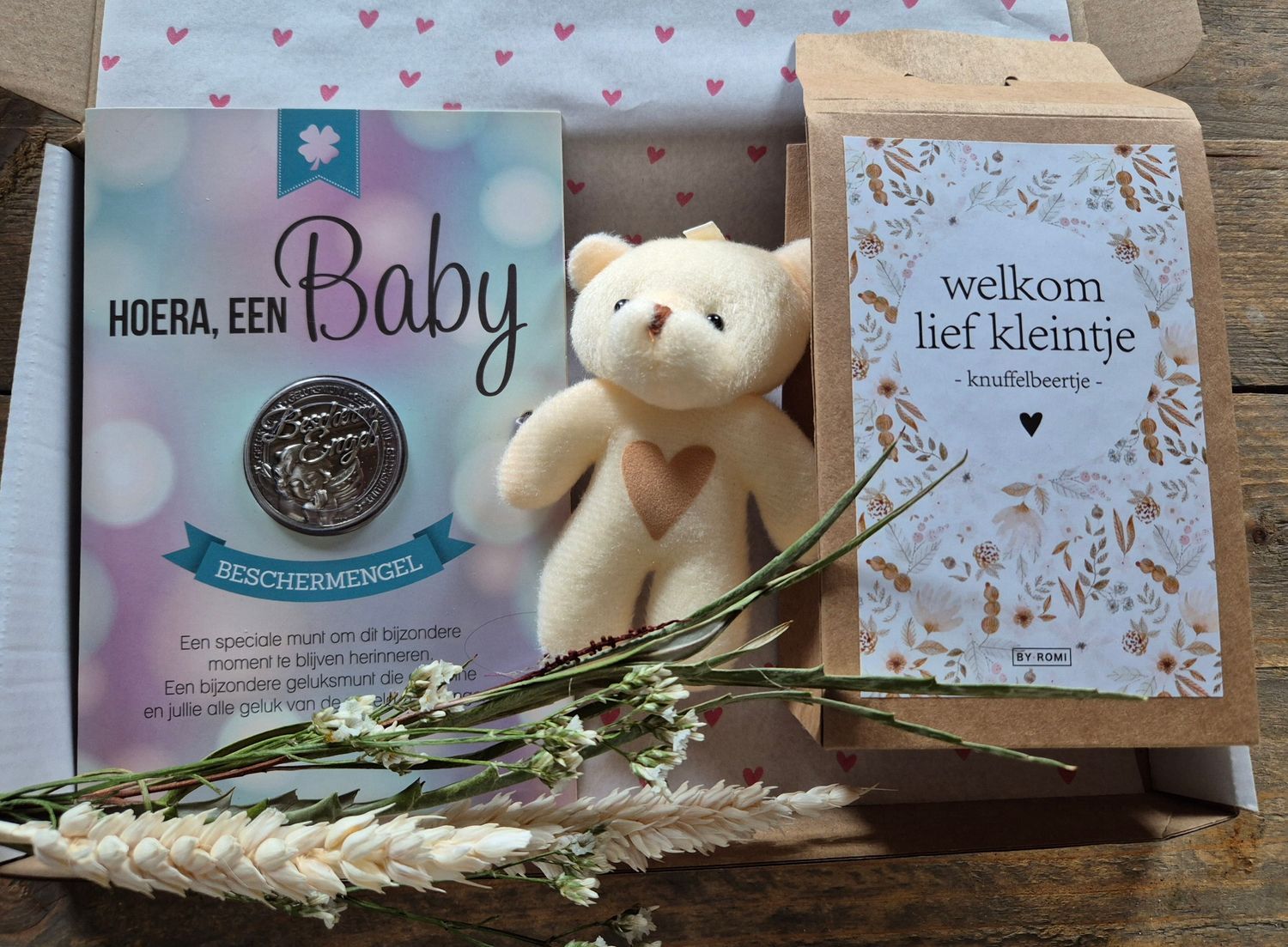 Babycadeauverpakking met teddybeer en Nederlandse wenskaarten op een versierde ondergrond.