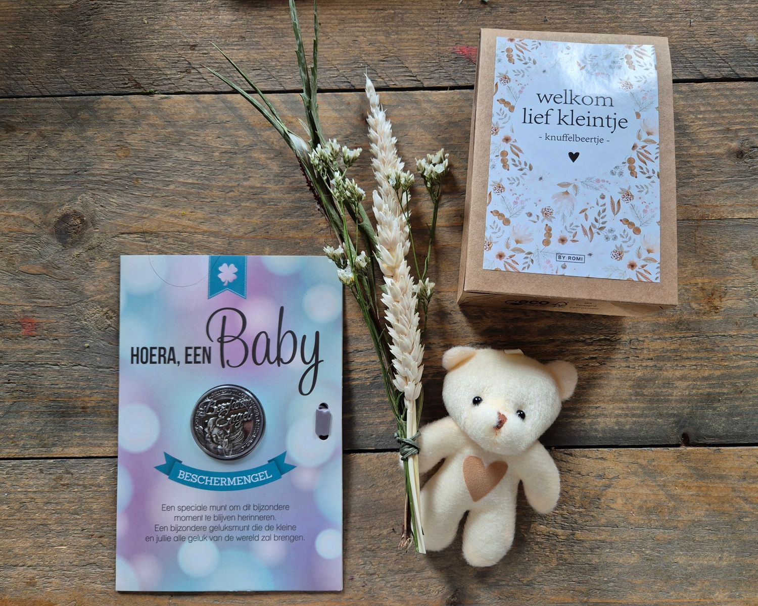 Babycadeauverpakking met teddybeer en Nederlandse wenskaarten op een versierde ondergrond.