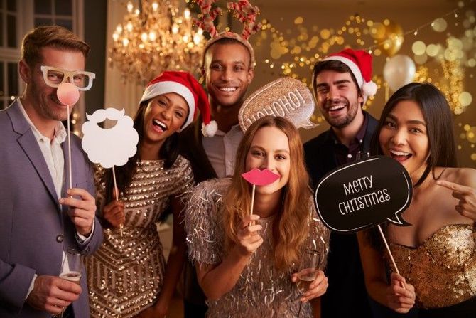 People at a festive holiday party holding props and a “Merry Christmas” sign