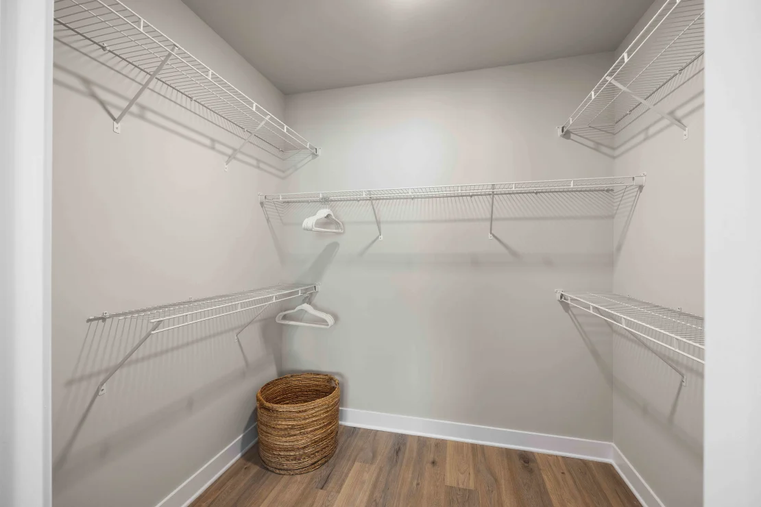 Walk-in closet with white wire shelves, hanging rods, and a basket on wood flooring.