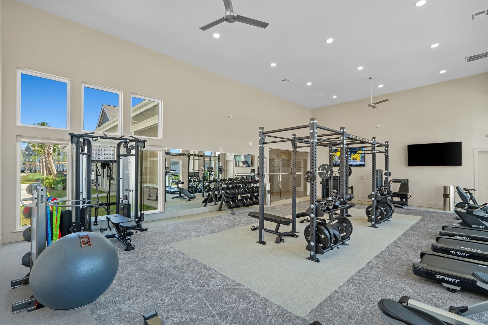 Bright community gym with weight racks, cardio machines, and a large mirrored wall.
