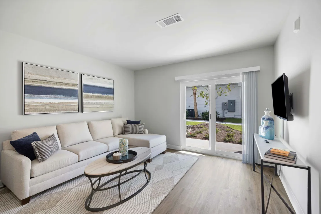 Bright living room with a beige sectional, coffee table, TV, and sliding glass door.
