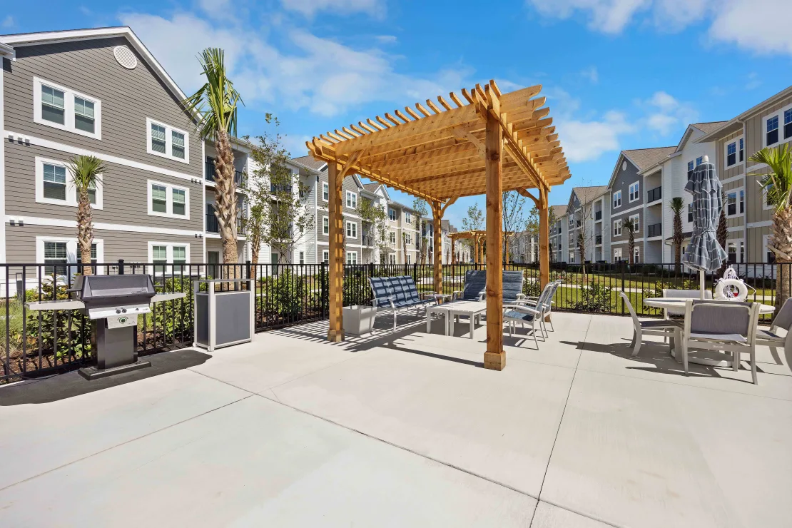 Outdoor communal patio with a wooden pergola, seating, and a grill in a multifamily community.