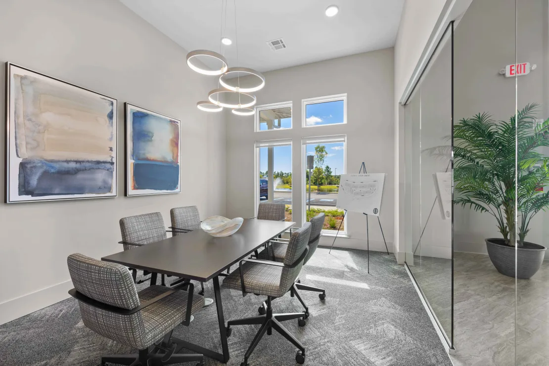 Modern conference room with glass walls, a long table, six chairs, abstract art, and a plant.