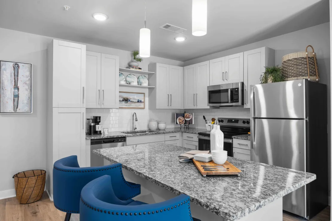Modern white kitchen with granite island, stainless steel appliances, and blue bar stools.