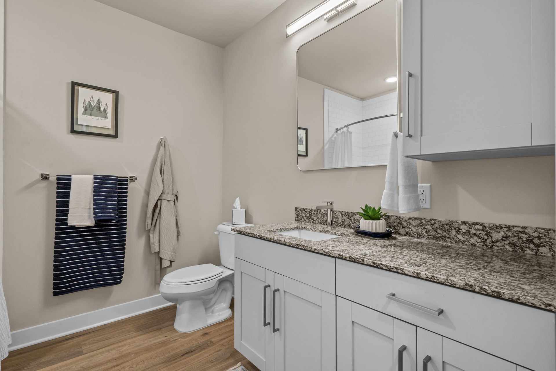 Modern apartment bathroom with granite countertop, white vanity, large mirror, and towel rack.