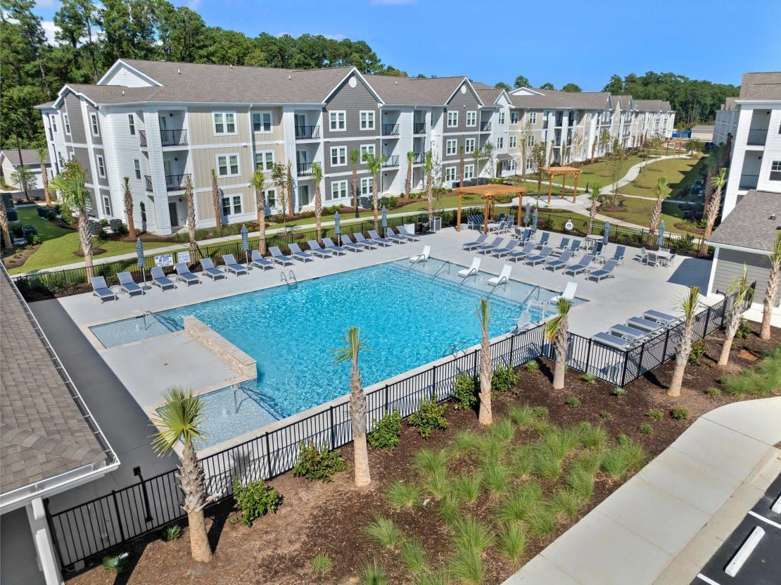 Outdoor community pool at an apartment complex with lounge chairs and landscaped surroundings.