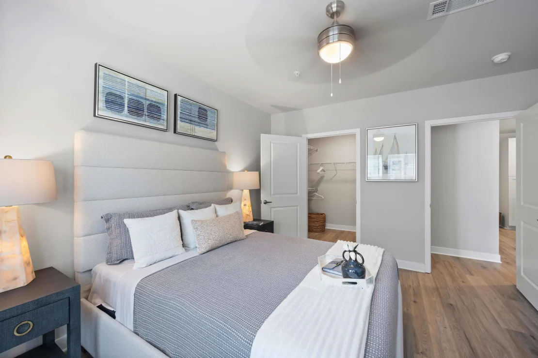 Bedroom in apartment with upholstered headboard, king bed, two matching nightstands, and open closet.