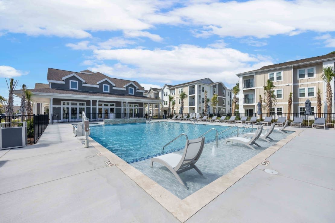 Outdoor pool area with lounge chairs and surrounding apartment buildings.