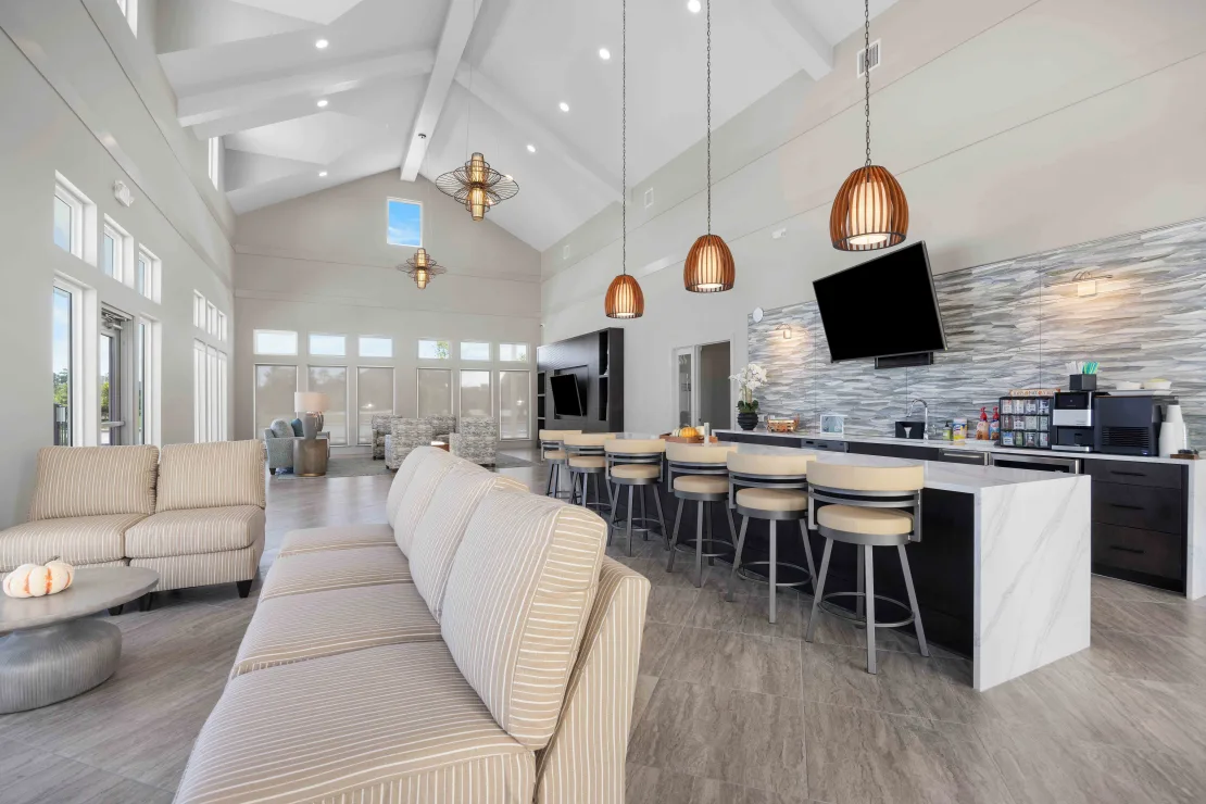 Bright modern community lounge with a long bar, couches, and high ceilings.