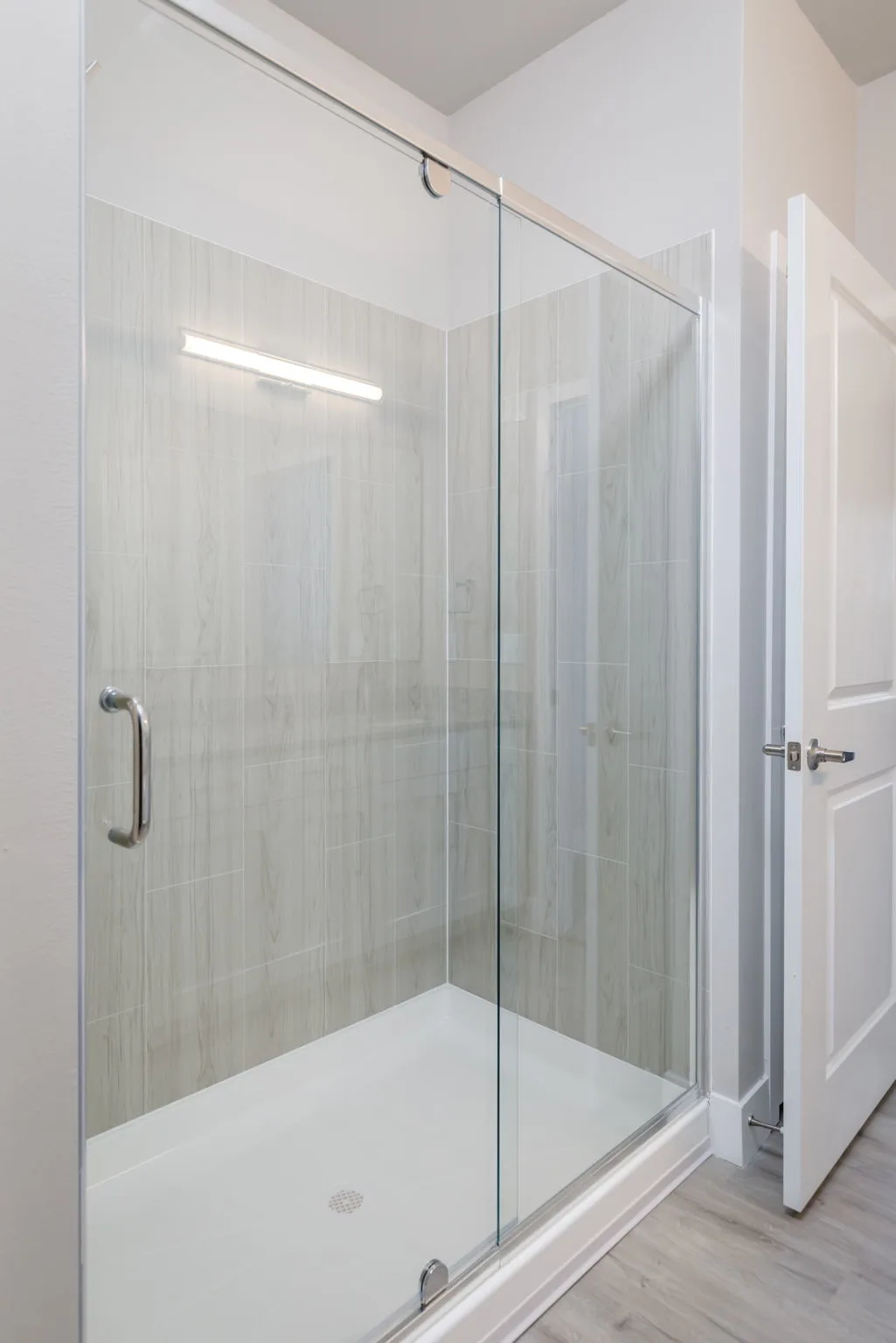 Glass sliding shower enclosure in a bright bathroom with light gray tile walls.