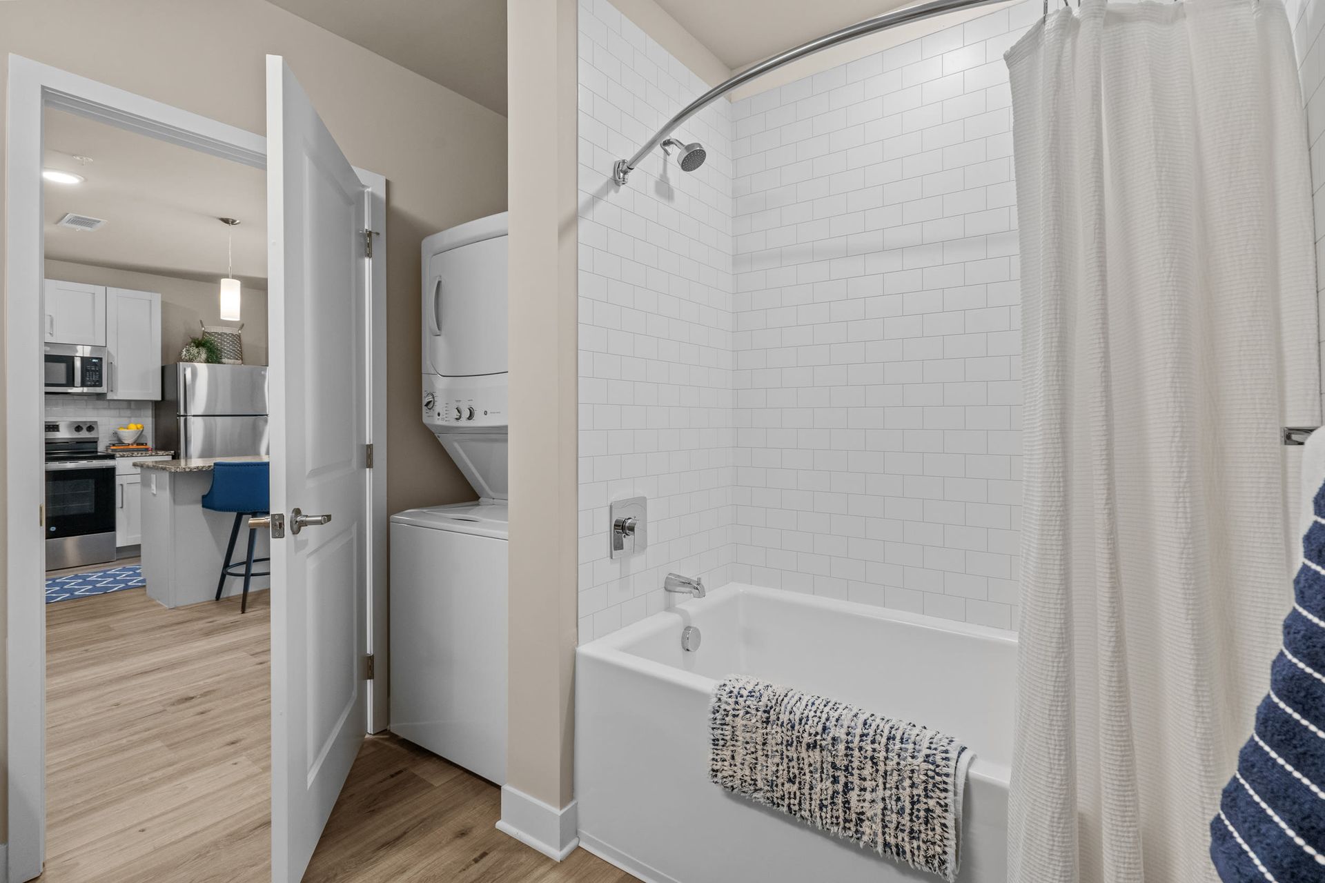 Stacked washer and dryer near a white-tiled bathtub in a modern apartment.