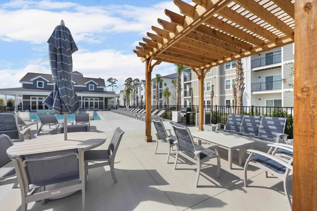 Outdoor apartment community pool deck with tables, chairs, and a wooden pergola.