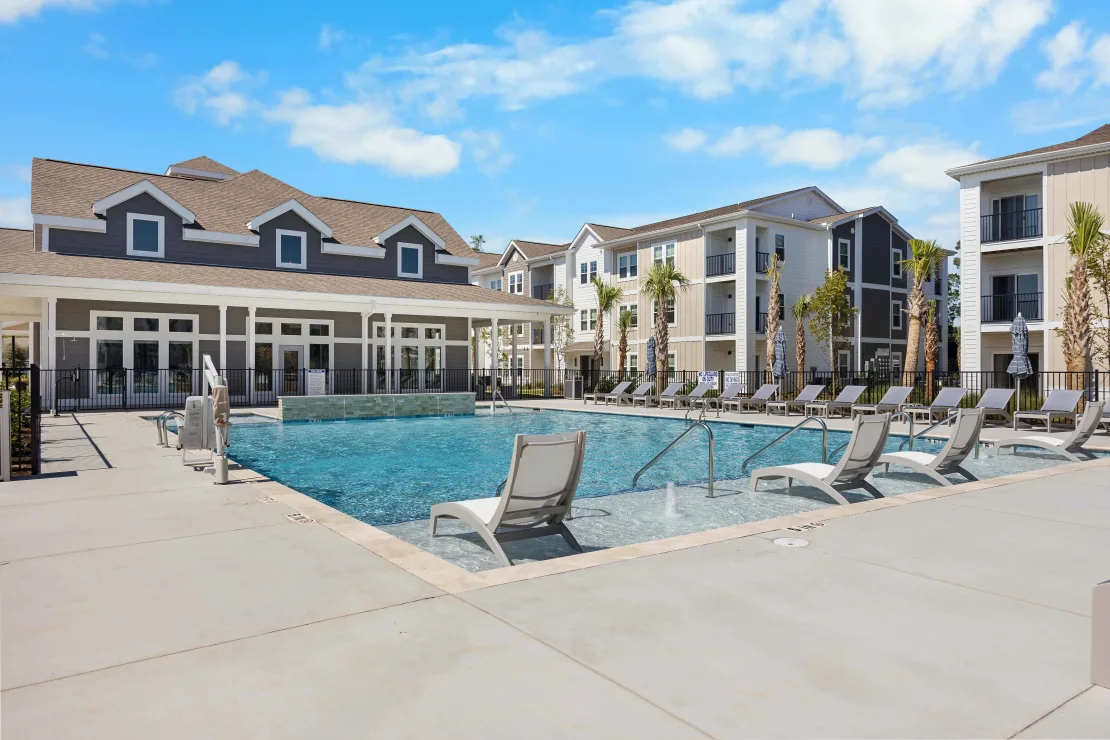 Outdoor pool at a multifamily community with lounge chairs and surrounding buildings.