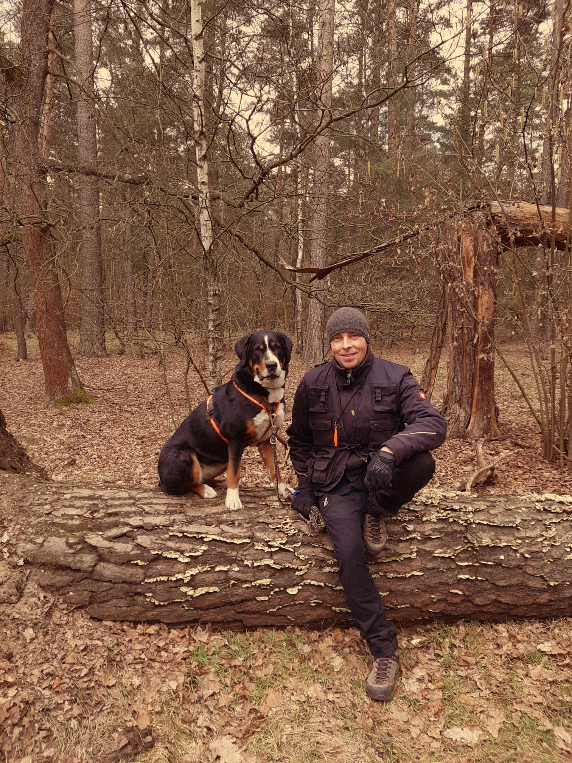 Oliver Kluge und sein Hund Elli sitzen auf einem Baumstamm im Wald.