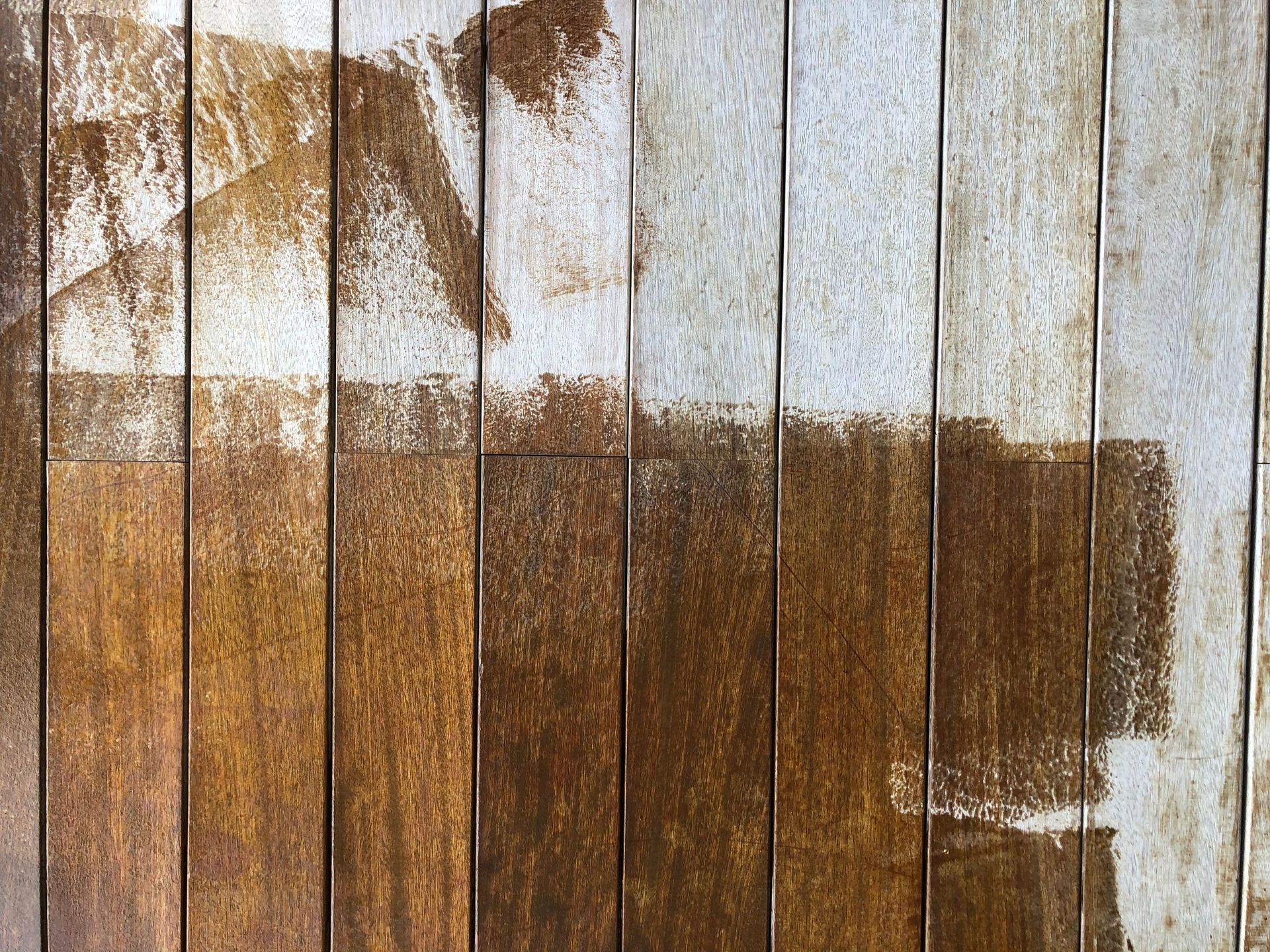 Weathered wooden fence with peeling white paint and large brown paint patches