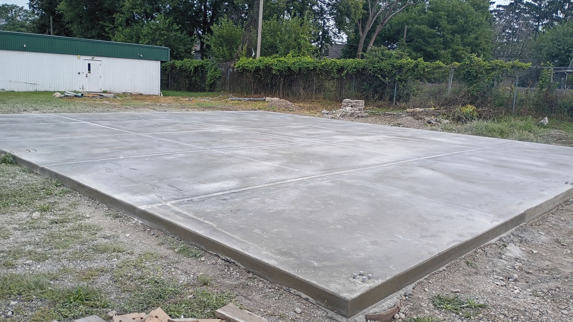Empty concrete slab in a grassy outdoor lot beside a small white building.