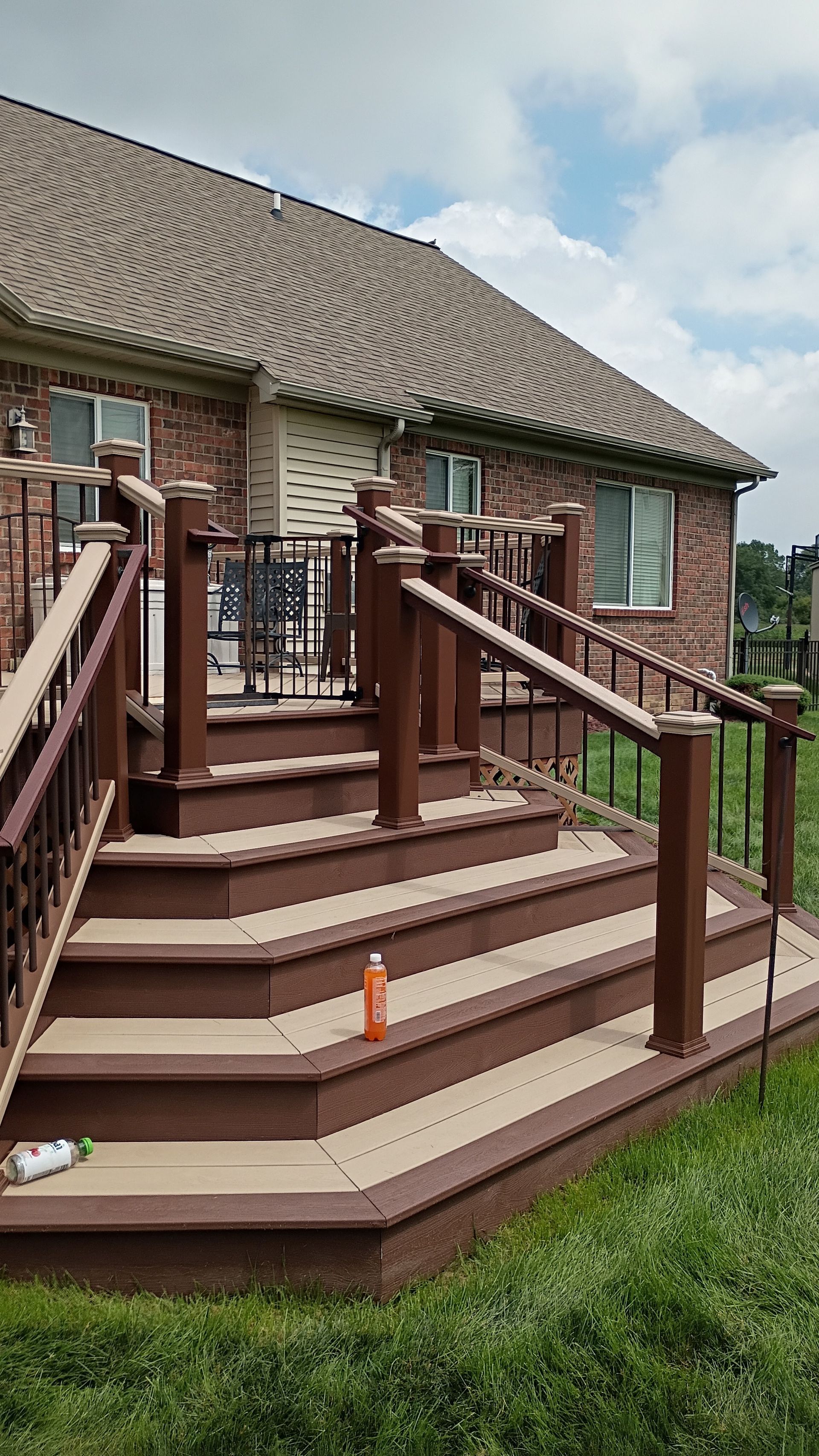 Front porch with brown wooden stairs and railings on a brick house under a cloudy sky