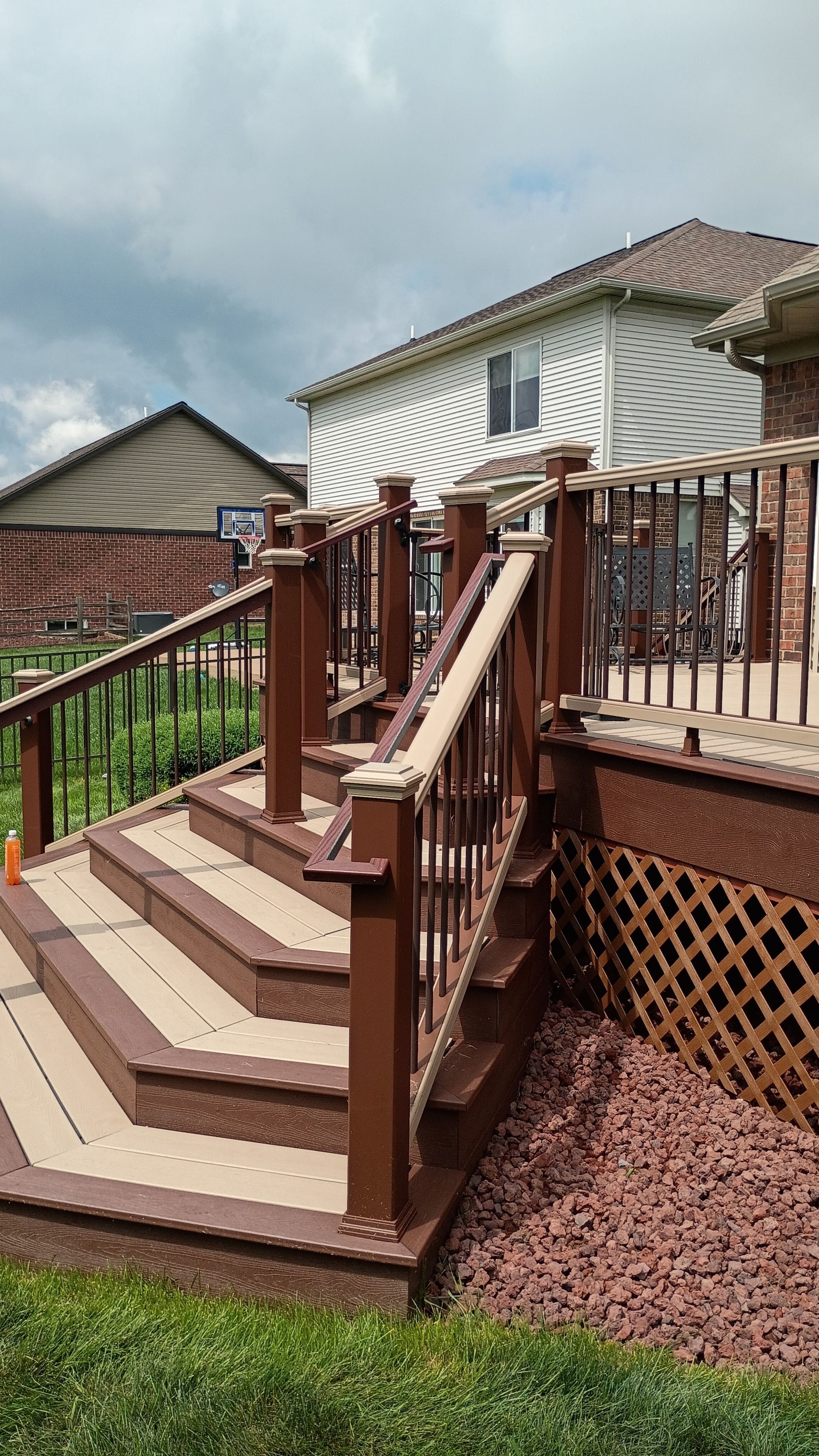 Wooden backyard deck stairs with railing beside a house, under cloudy skies