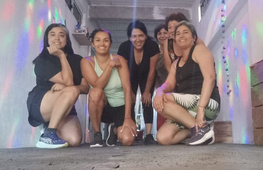 Grupo de mujeres posando juntas, algunas en cuclillas, en un espacio muy iluminado con luces de discoteca.