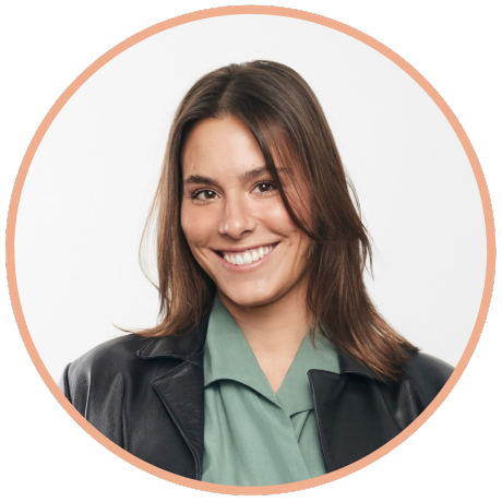 A smiling person with long dark hair, wearing a green collared shirt and black jacket, centered in a circular frame.