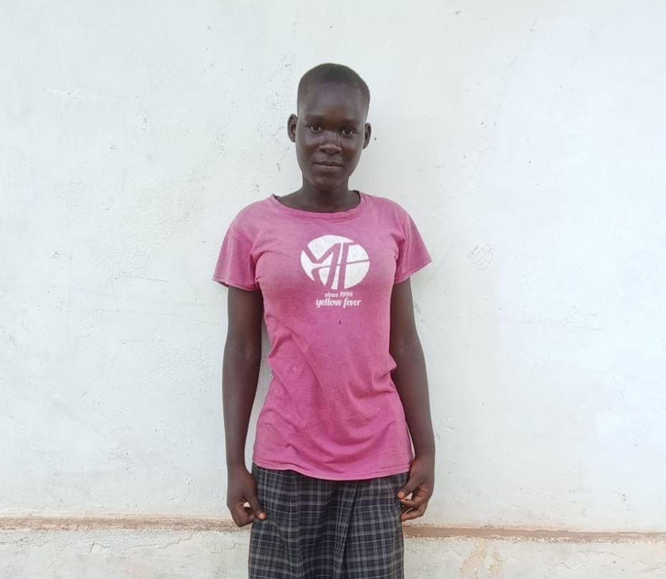Person in pink shirt and patterned pants stands in front of a white wall.