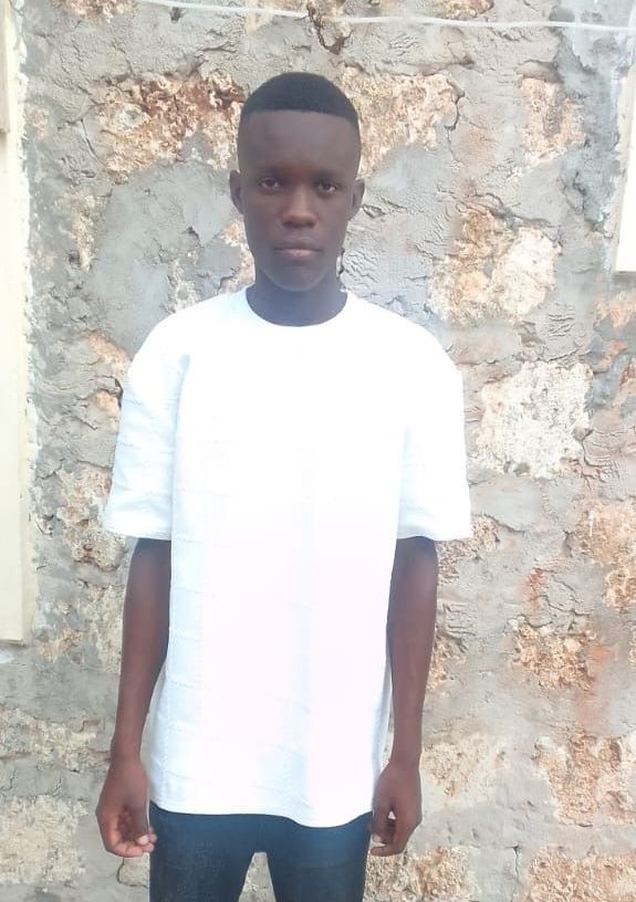 Man in white t-shirt stands in front of a textured stone wall.