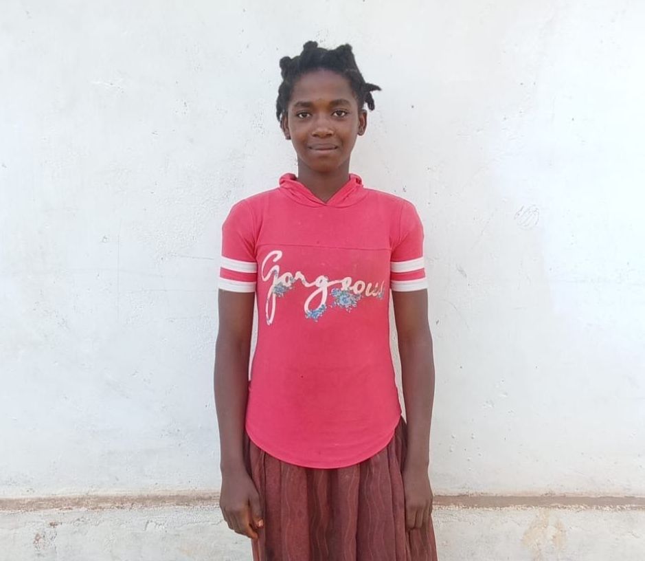 Woman in red top and brown skirt smiles in front of a white wall.