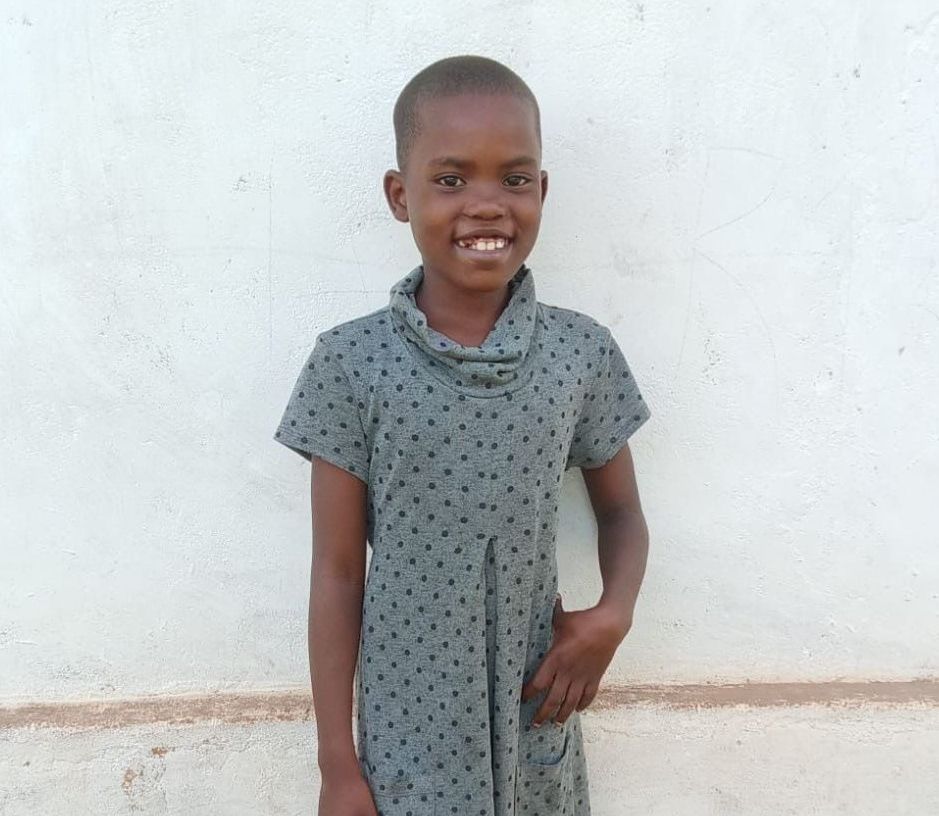 Girl in patterned dress smiles in front of a white wall.