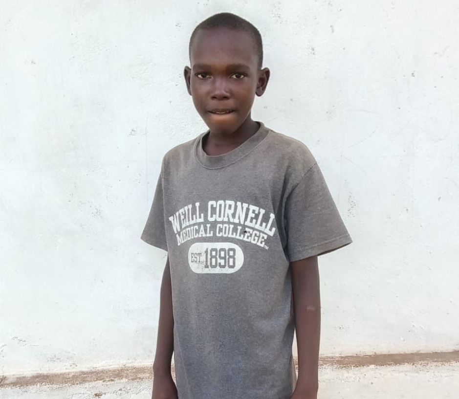 Boy wearing a gray shirt with text, standing in front of a white wall.