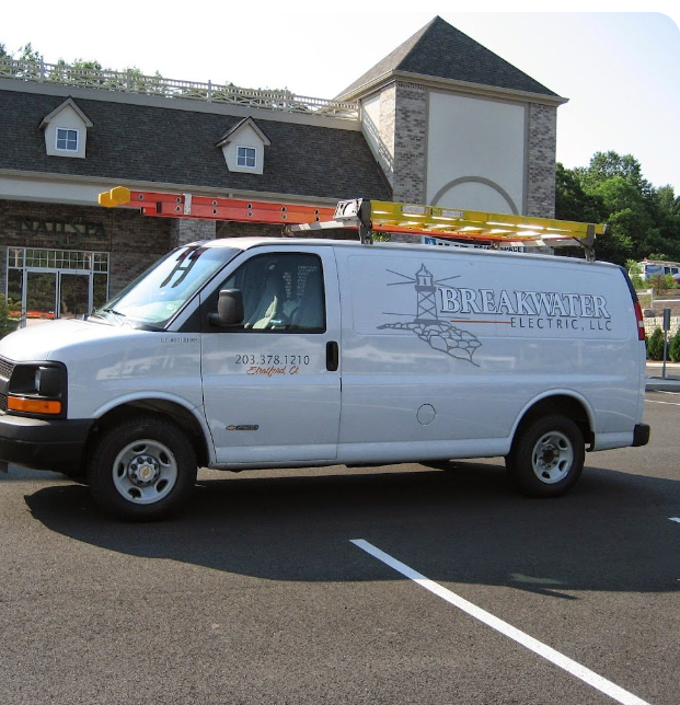 White utility van with ladders on top parked in a lot in front of a building