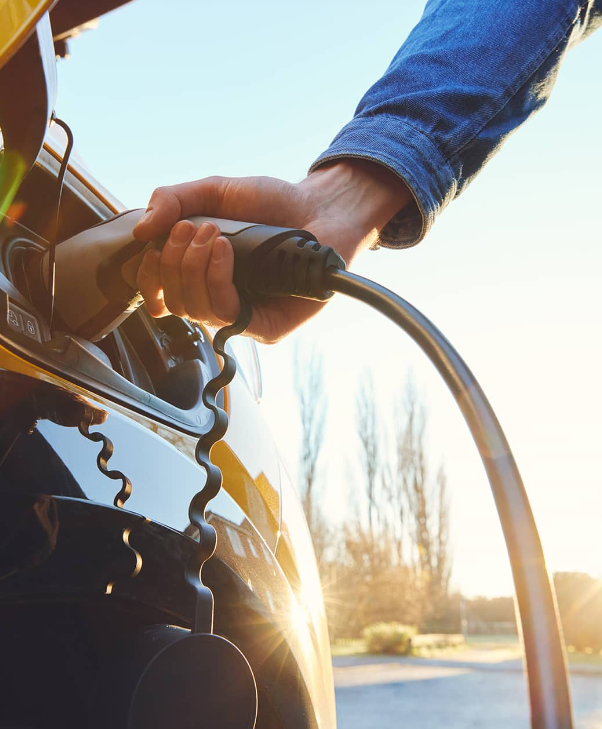 Hand plugging a charging cable into an electric vehicle at sunset
