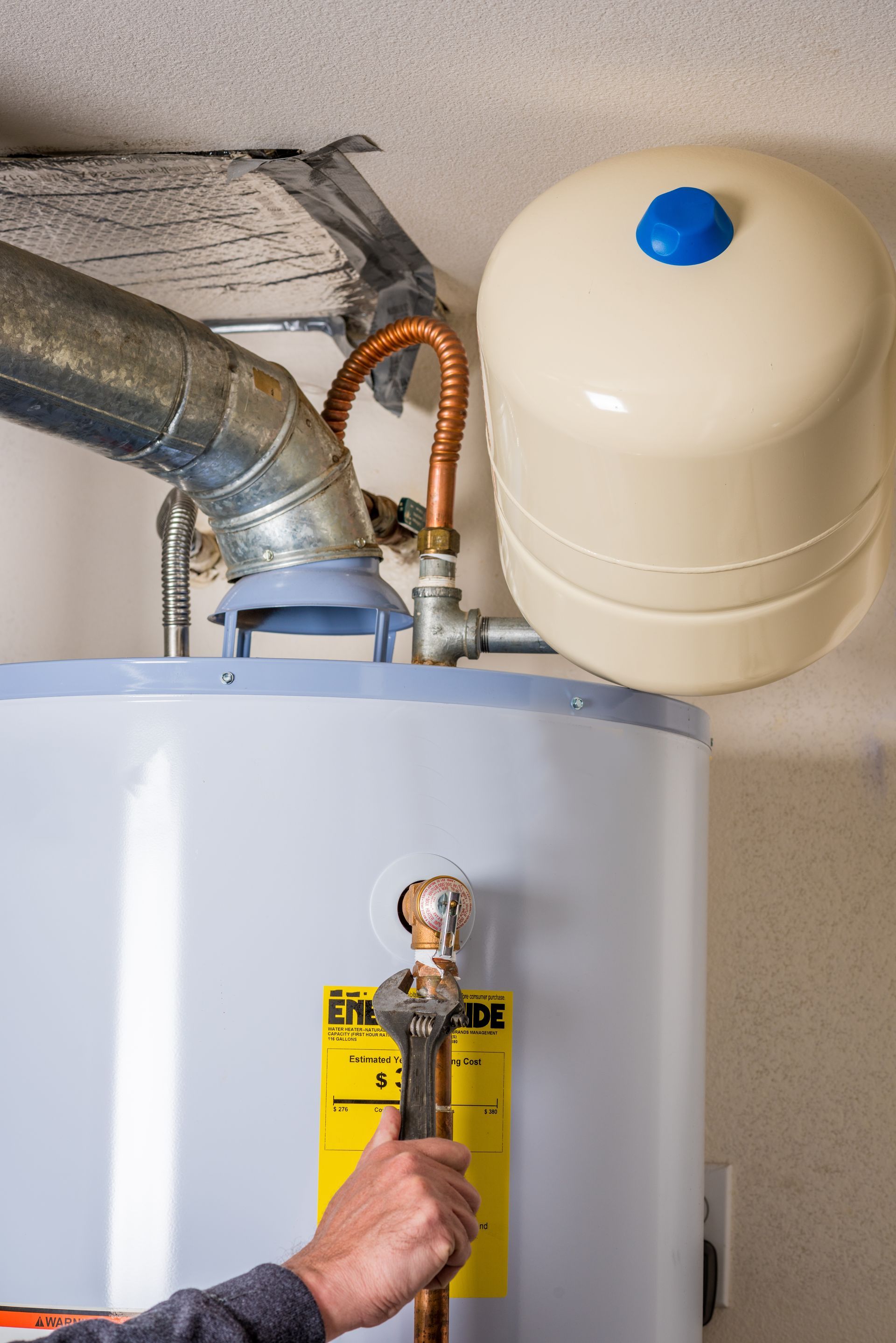 Hand holding a flashlight near a water heater, vent pipe, and expansion tank in a basement.