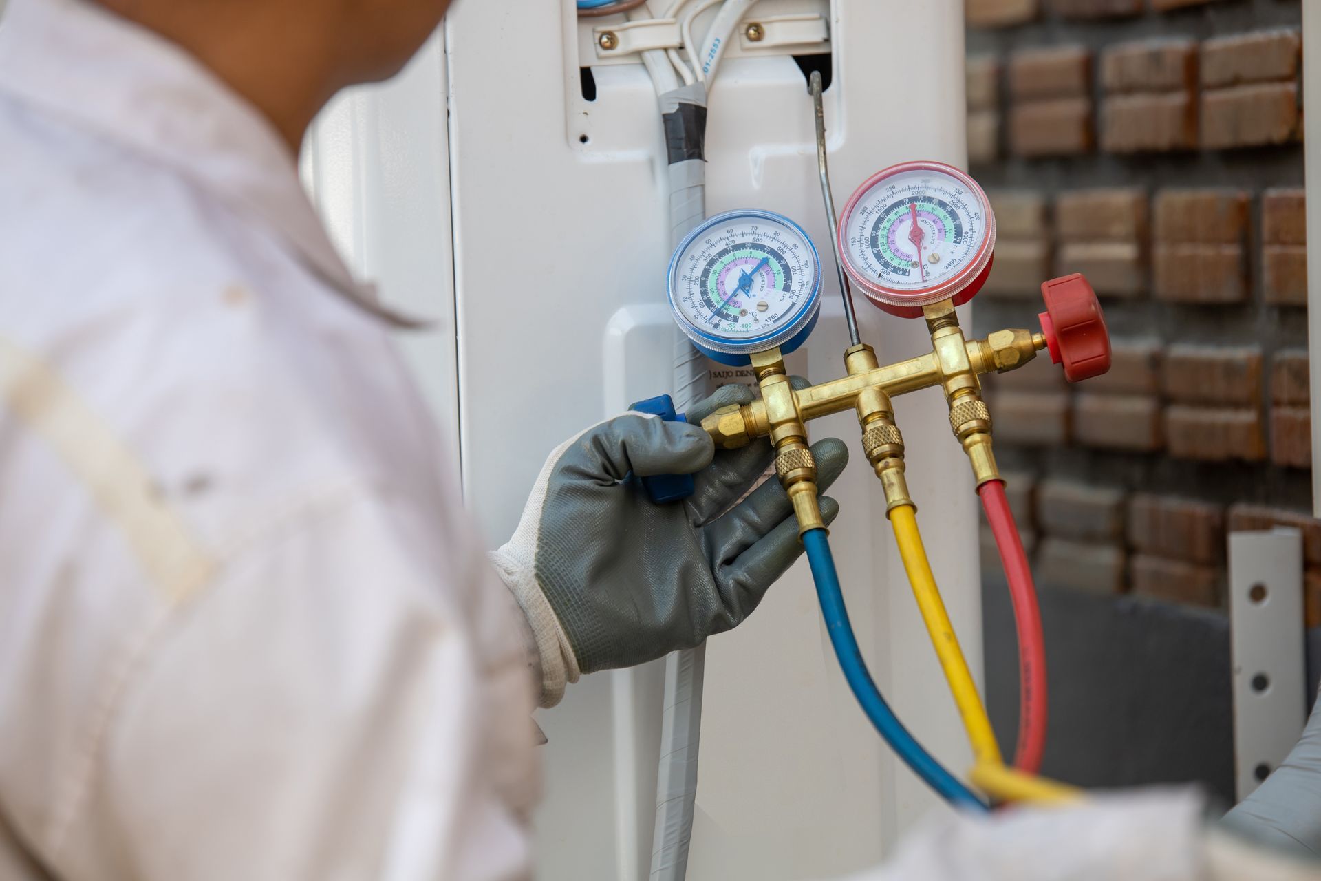 Technician checking HVAC manifold gauges on outdoor unit, with blue and red hoses attached