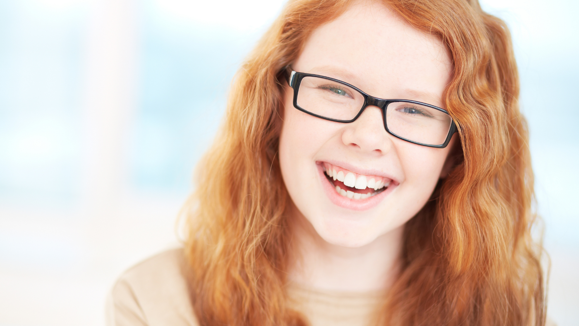Smiling red-haired person wearing glasses against a bright blurred background