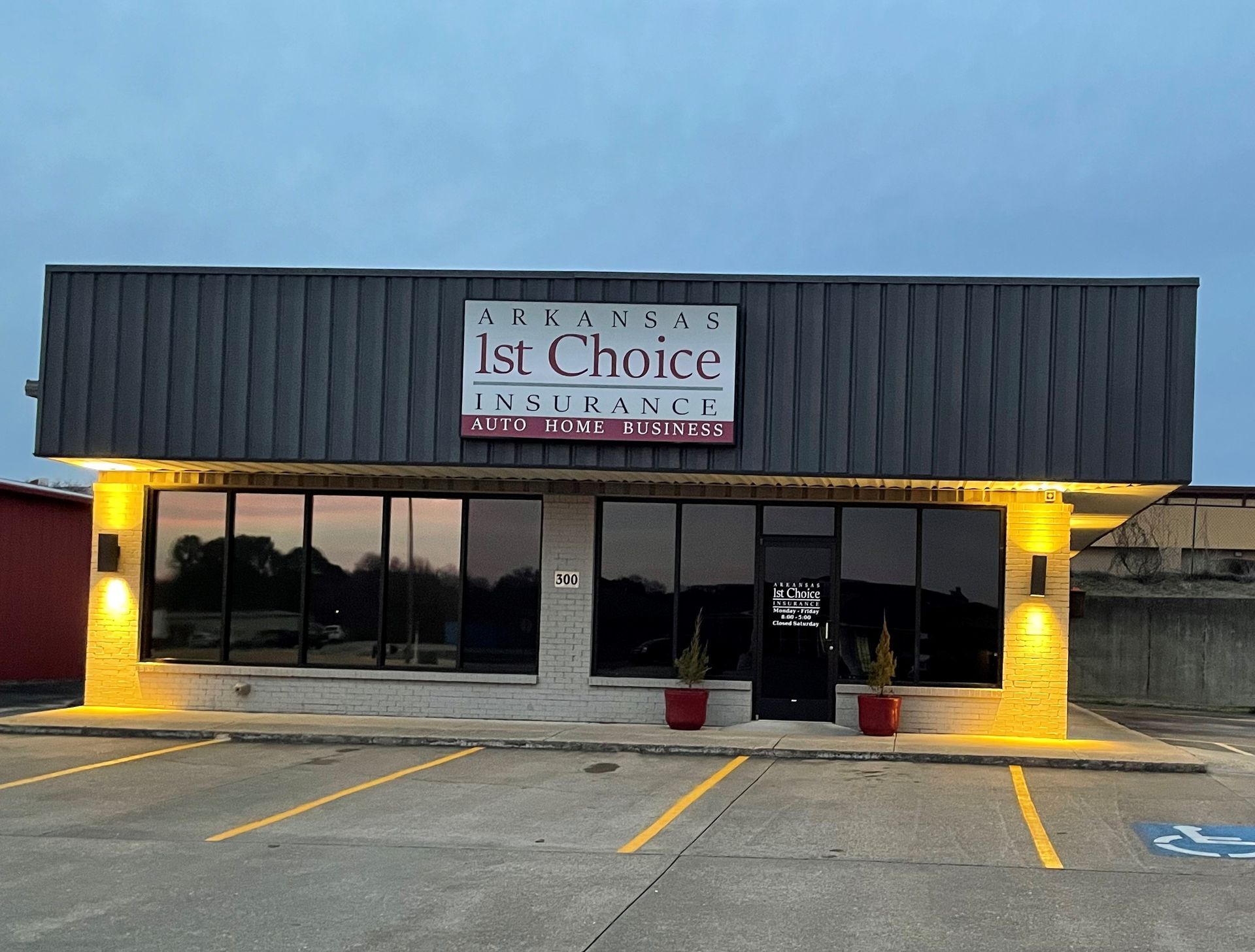 Arkansas 1st Choice Insurance Jonesboro office storefront with lit yellow columns and parking lot at dusk