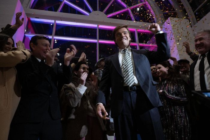 Man raising fist, celebrating with supporters, confetti, brightly lit interior.