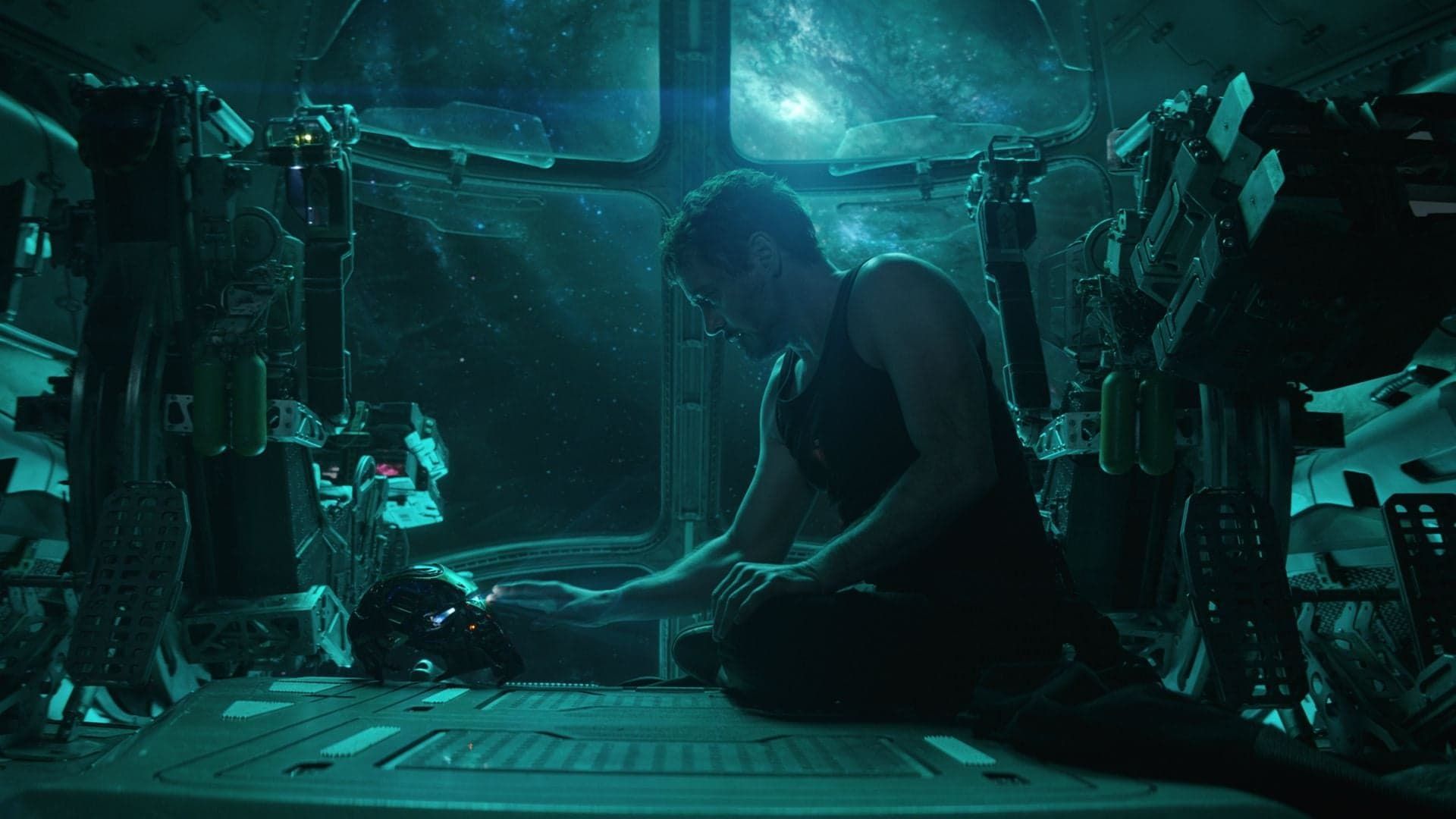 Person crouches in a dim teal-lit industrial room, working with equipment amid cables and machinery.