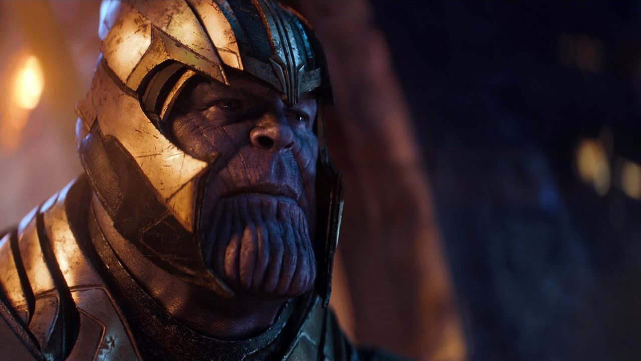 Close-up of Thanos in gold armor, lit by warm orange and blue light, staring sternly
