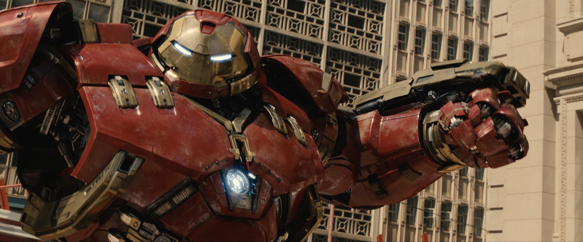 Iron Man in red-and-gold armor flying past city skyscrapers, arm raised to fire a weapon