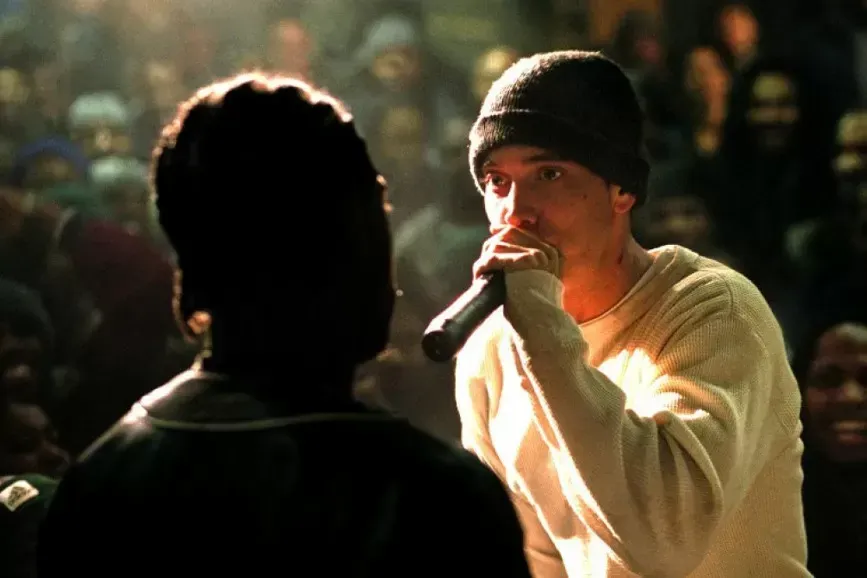Eminem rapping into a microphone in a rap battle, wearing a beanie.