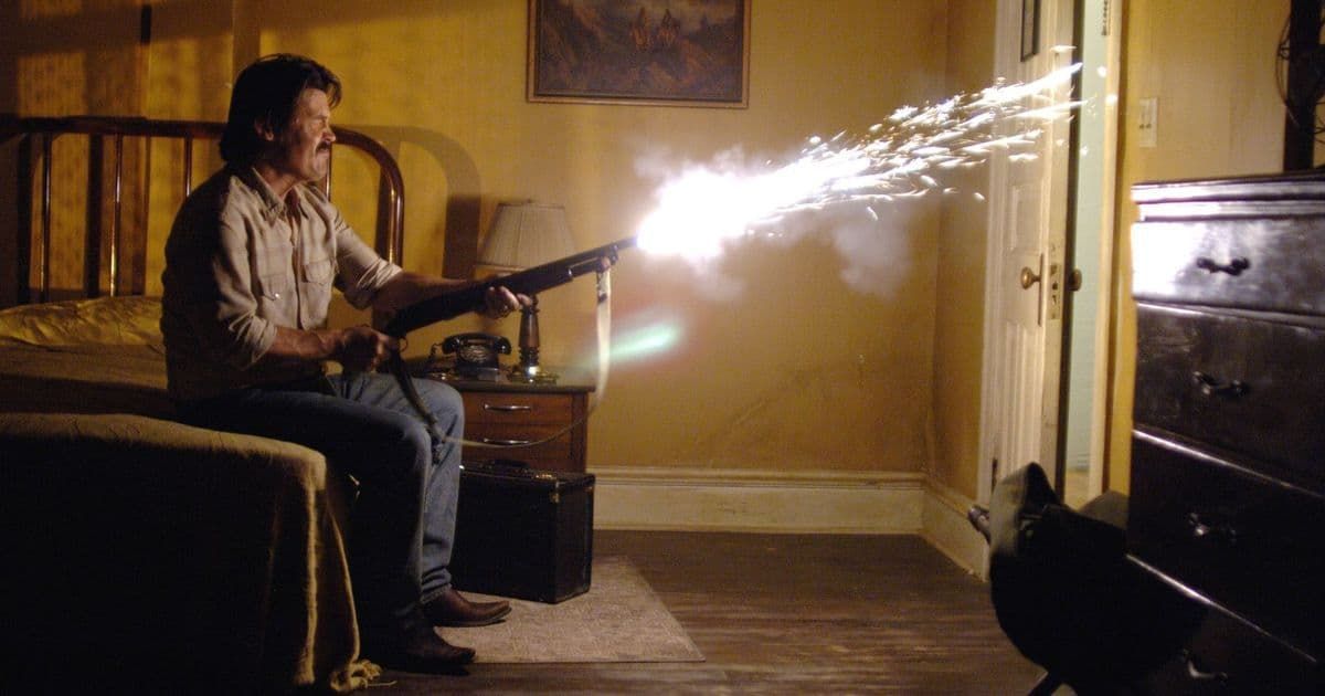 Person firing a shotgun indoors, bright muzzle flash lighting a dim room