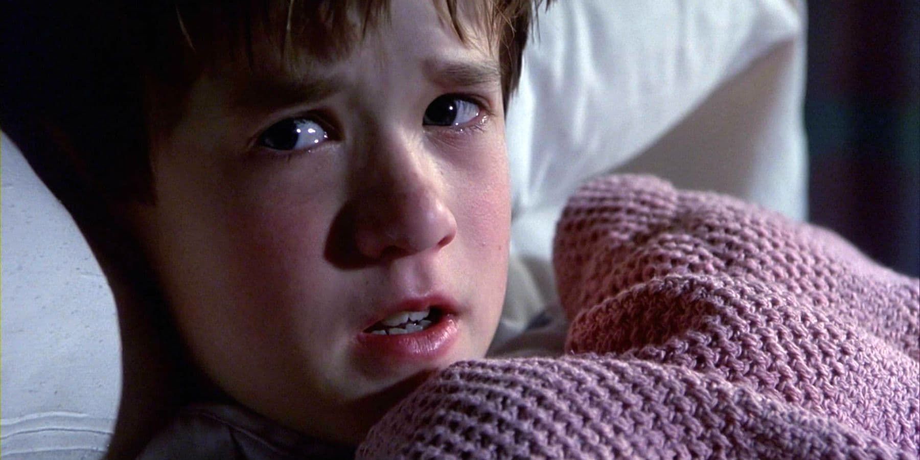 Close-up of a tearful child wrapped in a pink blanket, looking frightened in dim light