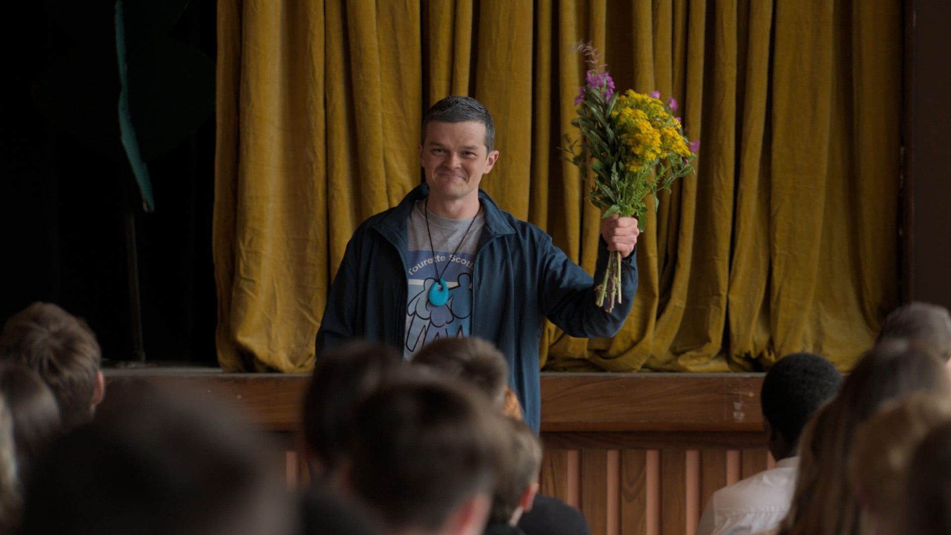 Person holding a bouquet stands behind a podium, addressing an audience in a dimly lit room.