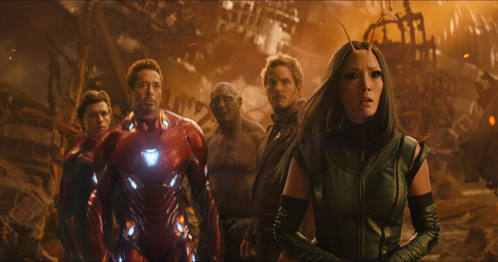 Superhero team standing in a fiery, industrial setting, with Iron Man glowing at center and a woman in green at right