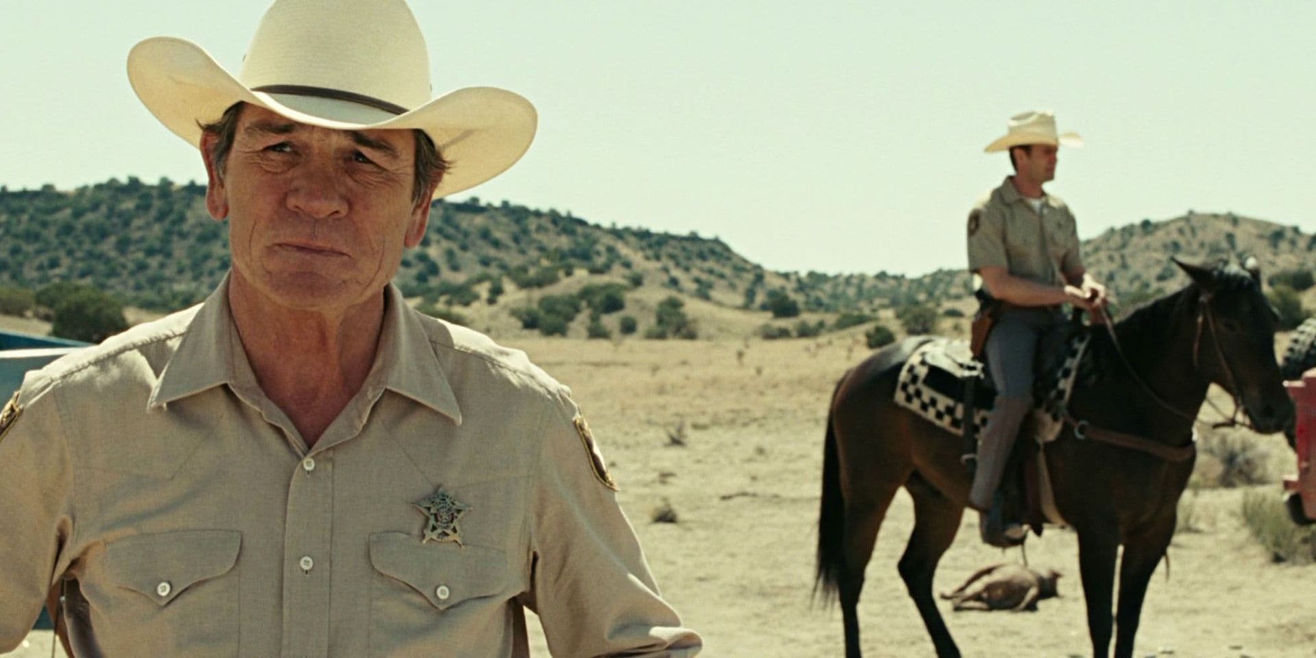 Cowboy in white hat stands in desert foreground, with another rider on horseback behind him.