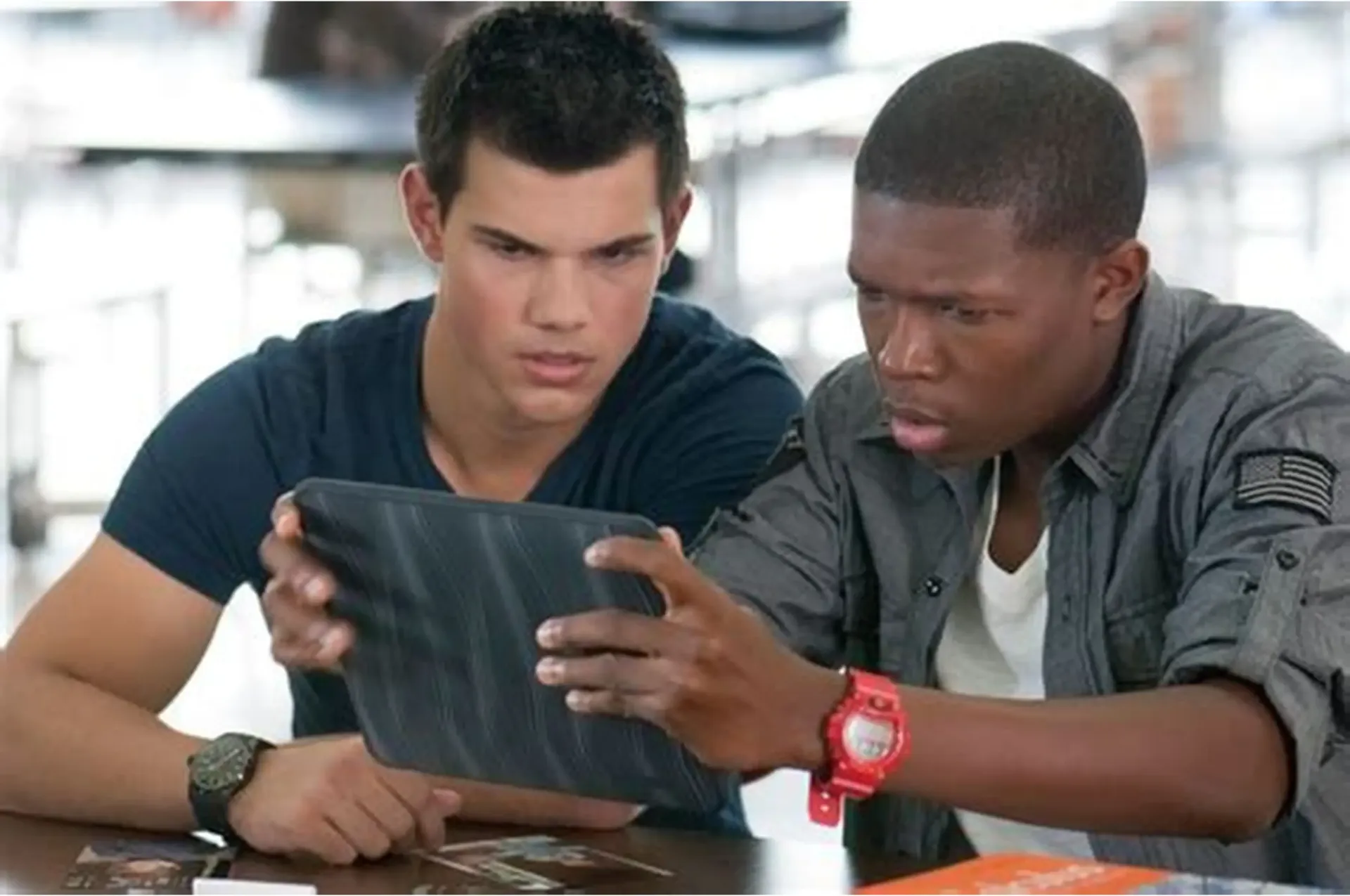 Two young men looking intently at a tablet computer. Indoors, at a table.