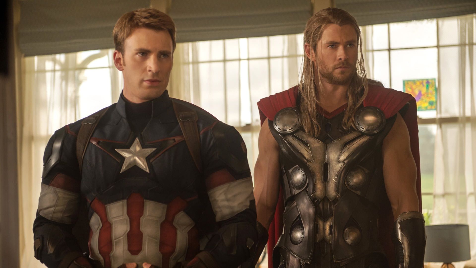 Two armored superheroes stand indoors, one in a star-emblazoned suit, the other holding a hammer.